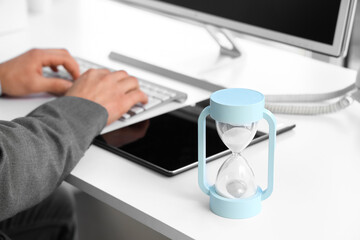 Hourglass on desk against businessman working with computer in office, closeup
