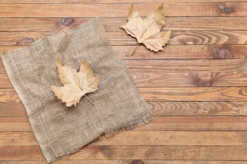 Burlap cloth with dried leaves on wooden background