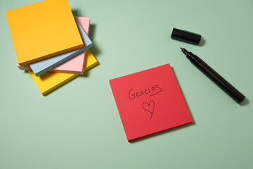 Red sticky note with "Gracias" and heart drawing on pastel background