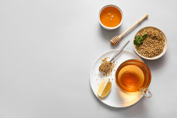 Glass cup of hot buckwheat tea with lemon, mint and bowl of honey on grey background