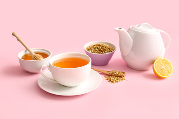 Cup and teapot of hot buckwheat tea with lemon and bowl of honey on pink background