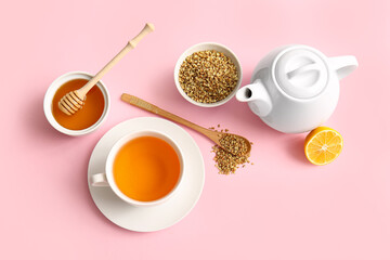 Cup and teapot of hot buckwheat tea with lemon and bowl of honey on pink background