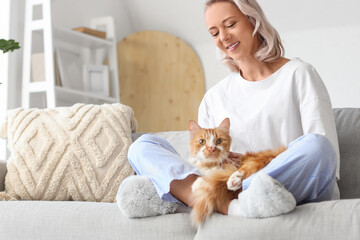 Beautiful woman in soft slippers with cute cat sitting on sofa at home