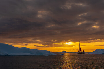 Disko bay western coast of Greenland at sunset with red sailboat