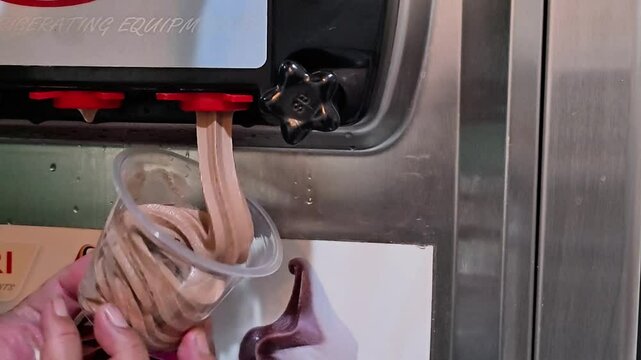 Close up shot of a worker swirling Chocolate soft ice cream with machine into a plastic cup. Ice cream maker machine making soft serve ice cream.