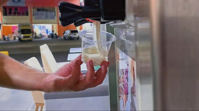 Making twist Vanilla ice cream with machine. Ice cream maker swirling soft serve ice cream into take away plastic cup. Frozen yoghurt, cold and healthy dessert.