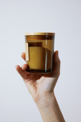 Hand holding a candle on white background with wooden lid and stopper