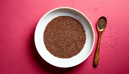 Top view of chia seeds in a white plate with a spoon on a pink background