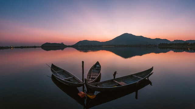 Three wooden boats lay silently reflecting on the calm lake surface
