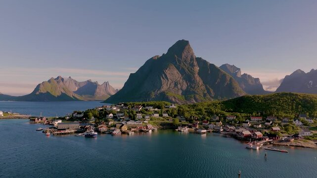 Explore a picturesque coastal village in Norway nestled between majestic mountains and tranquil waters. The sun casts a warm glow, Reine village Lofoten