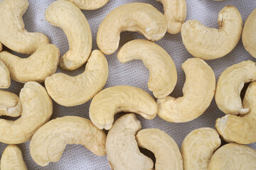 A close-up macro photograph of a handful of raw cashew nuts isolated on a white background, showcasing their natural texture, creamy color, and detailed surface. Perfect for concepts related to health