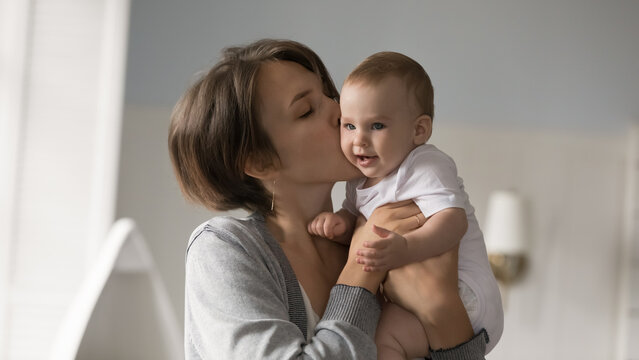Tenderness and care. Family portrait caring loving young single parent mom hug cuddle hold in arms healthy smiling little infant kiss plumpy son or daughter cheek feel emotional bonding with baby kid