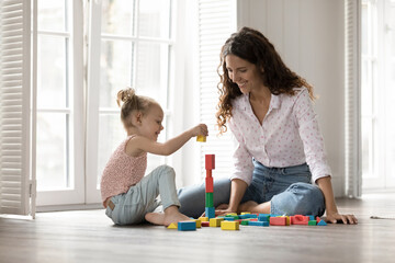 Interactive playtime. Happy young female mom teacher nanny psychologist play toy blocks with little...