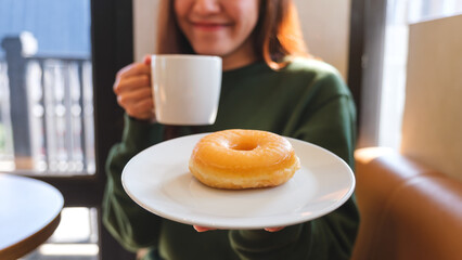 Closeup of a young woman holding and drinking hot coffee and eating donut in cafe