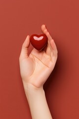 A passionate gesture symbolizes love, as a hand cradles a vibrant red heart against a bold crimson backdrop, evoking warmth and affection.