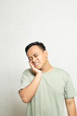 portrait of the body of an adult male holding one cheek due to a toothache, dressed in sage clothing.