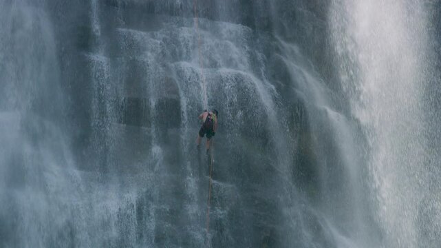 Person slowly rappelling down massive, misty, rocky waterfall - cinematic 