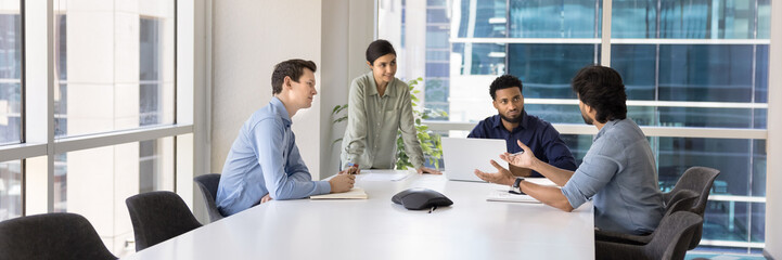 Wide shot of young diverse business colleagues working on project together in meeting room, talking...