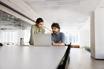 Couple of young Indian professional colleagues working on online project together, talking at...