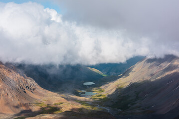 Aerial top view to green rocky hilly valley with two turquoise lakes under lush low clouds. Most...