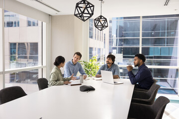 Diverse group of professional colleagues talking at large white table in conference room,...