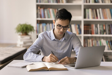 Doing homework. Focused male teenager in eyewear write literature review at college university...