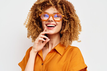 Smiling woman with curly hair wearing stylish glasses, posing against a light background,...