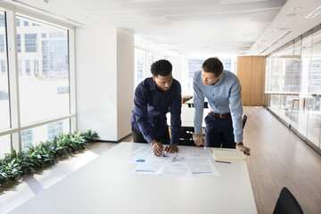 Focused busy multiethnic male professionals working on project reports together, analyzing...