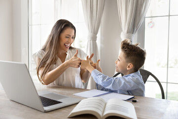 Happy proud mom and successful schoolkid son bumping thumbs up like hands at kids learning table, sitting at laptop, open books, celebrating educational progress, completed homework, high grades