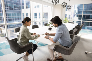 Two Indian business colleagues discussing job case at meeting table, talking in collaboration room,...