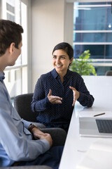 Cheerful young Indian business professional woman talking to male coworker, explaining creative...