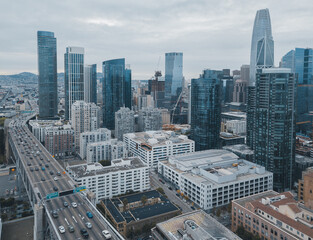 Fototapeta premium Aerial view of modern skyscrapers and busy freeway in downtown San Francisco under an overcast sky.