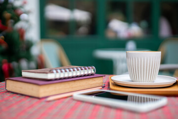 Coffee cup with book for read and mobile phone,  diary book on table at outdoor cafe in the morning