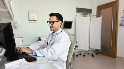 Focused positive ultrasound diagnosis doctor working at computer alone in clinic examination room, typing scanning checkup report, using digital technology for medical job. Banner shot