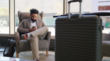 A stylish traveler relaxes in a sleek chair with his smartphone, while a fashionable suitcase rests nearby, embodying the contemporary aesthetics and sophistication of modern travel