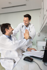 Obraz premium Two cheerful practitioner doctor making high five gesture, smiling, laughing, celebrating professional medical success, enjoying teamwork, collaboration. Vertical shot