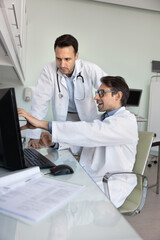 Positive Latin doctor man in white coat showing electronic medical report, scanning result to male colleague, consulting ultrasound diagnosis specialist, pointing at monitor in examination room