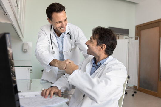 Two happy male doctors giving high five at workplace in clinic office, lab, examination room, joining hands in support motivation gesture, enjoying good teamwork result, successful cooperation