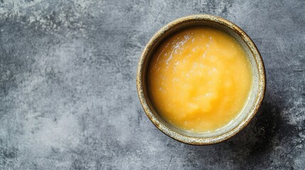 Overhead shot of a rustic bowl filled with creamy applesauce on a textured gray background ideal for food related content.