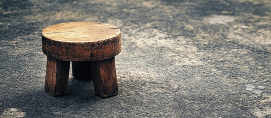 Naklejka premium Rustic wooden stool featuring rich brown tones on a textured asphalt background perfect for outdoor decor and artistic photography compositions