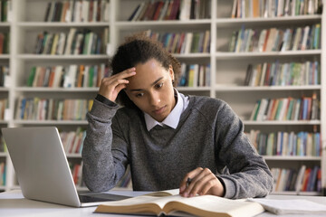 Book is source of knowledge. Serious thoughtful young hipster guy university student engaged in reading paper textbook at library desk learn new information from education literature study materials