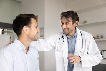 Happy cheerful Latin medical specialist expressing support to positive patient, touching back of...