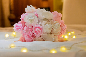 romantic hotel room scene with a beautiful bouquet of flowers placed elegantly on the bed. The soft petals of the flowers are surrounded by twinkling string lights, creating a warm and inviting