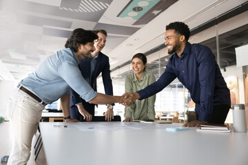 Cheerful positive multiethnic business colleagues celebrating corporate success, shaking hands over...