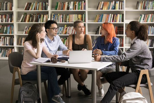 Teamwork learning. Multiethnic teenage students gather in library around table with notebook discuss online video class collaborate on group project listen to female leader setting tasks to groupmates