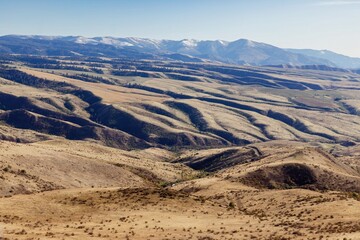 High angle view of a mountain range with rolling hills and valleys. Patches of snow on the distant peaks. A winding road is visible. , White Bird, Idaho, USA.