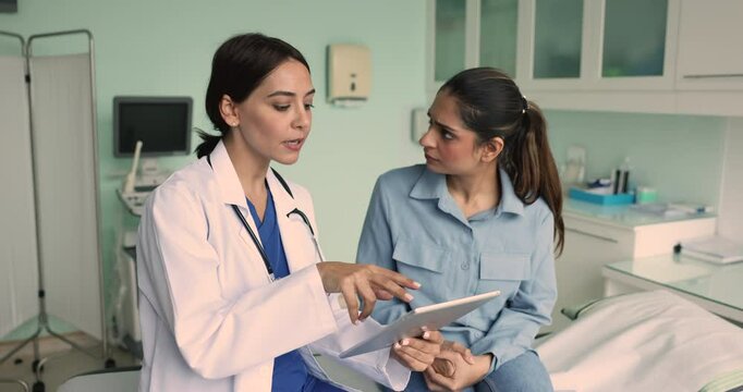 Focused young Middle Eastern doctor and Indian patient reviewing and discussing ultrasound examination results on tablet, getting cheerful, positive, shaking hands in clinic sonographer room