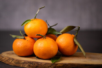 A pile of whole mandarine fruits with leaves on wooden plate, grey table background