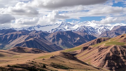 Majestic snow-capped mountain range overlooking a vast, undulating landscape of rolling hills and valleys under a partly cloudy sky.