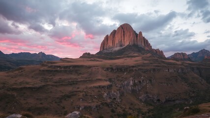 Majestic mountain peak at sunset, dramatic pink clouds over rugged terrain in caucasus mountains.